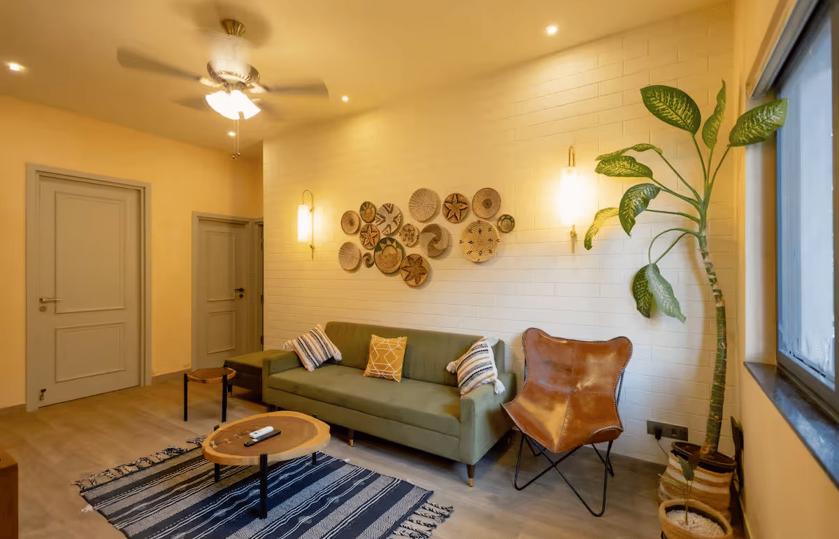 A cosy living room with a cushioned sofa, a small round table on a carpet, warm lighting, and indoor plants at Lime Tree Villa with Private Pool | Luxury Stay in Goa.